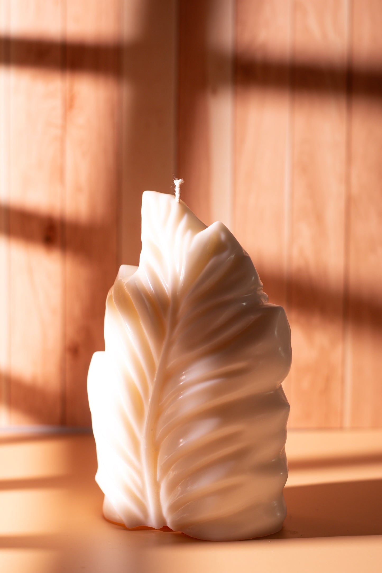 Handcrafted feather-shaped sculpted candle by JAL Candles, made from soy wax and photographed in warm natural light on a wooden surface in Cyprus.