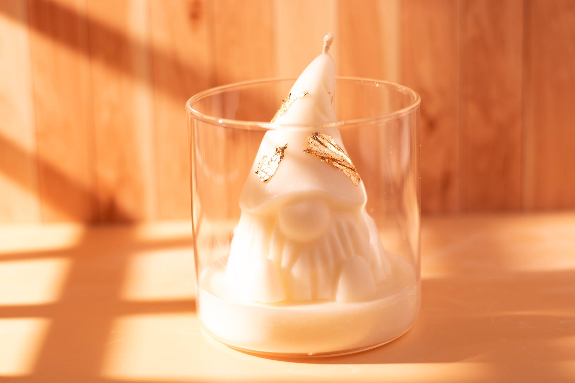 White sculpted Christmas gnome candle with gold leaf details in a glass jar, photographed on a wooden background
