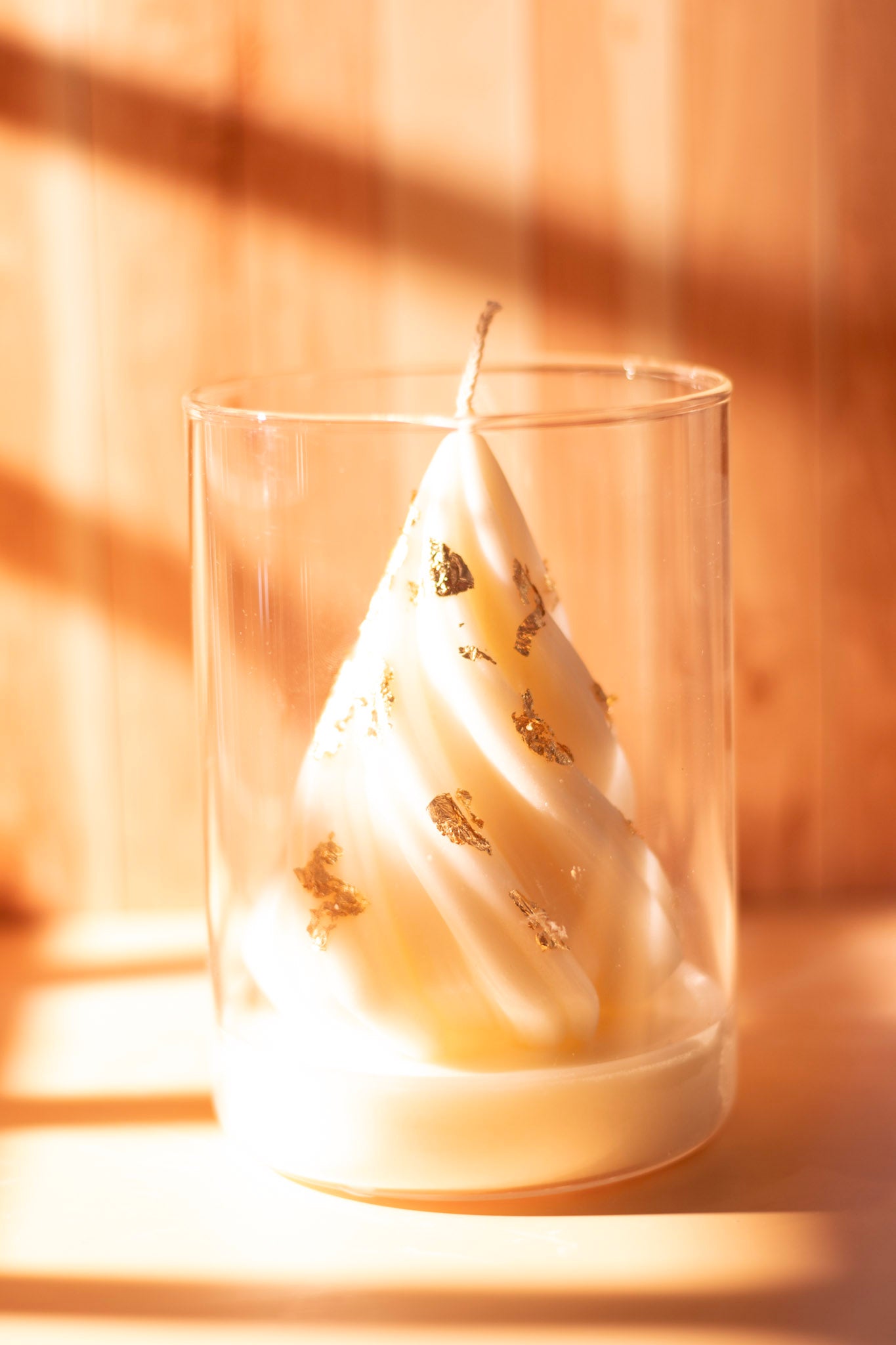 White sculpted Christmas tree candle with gold leaf accents in a clear glass jar on a wooden background