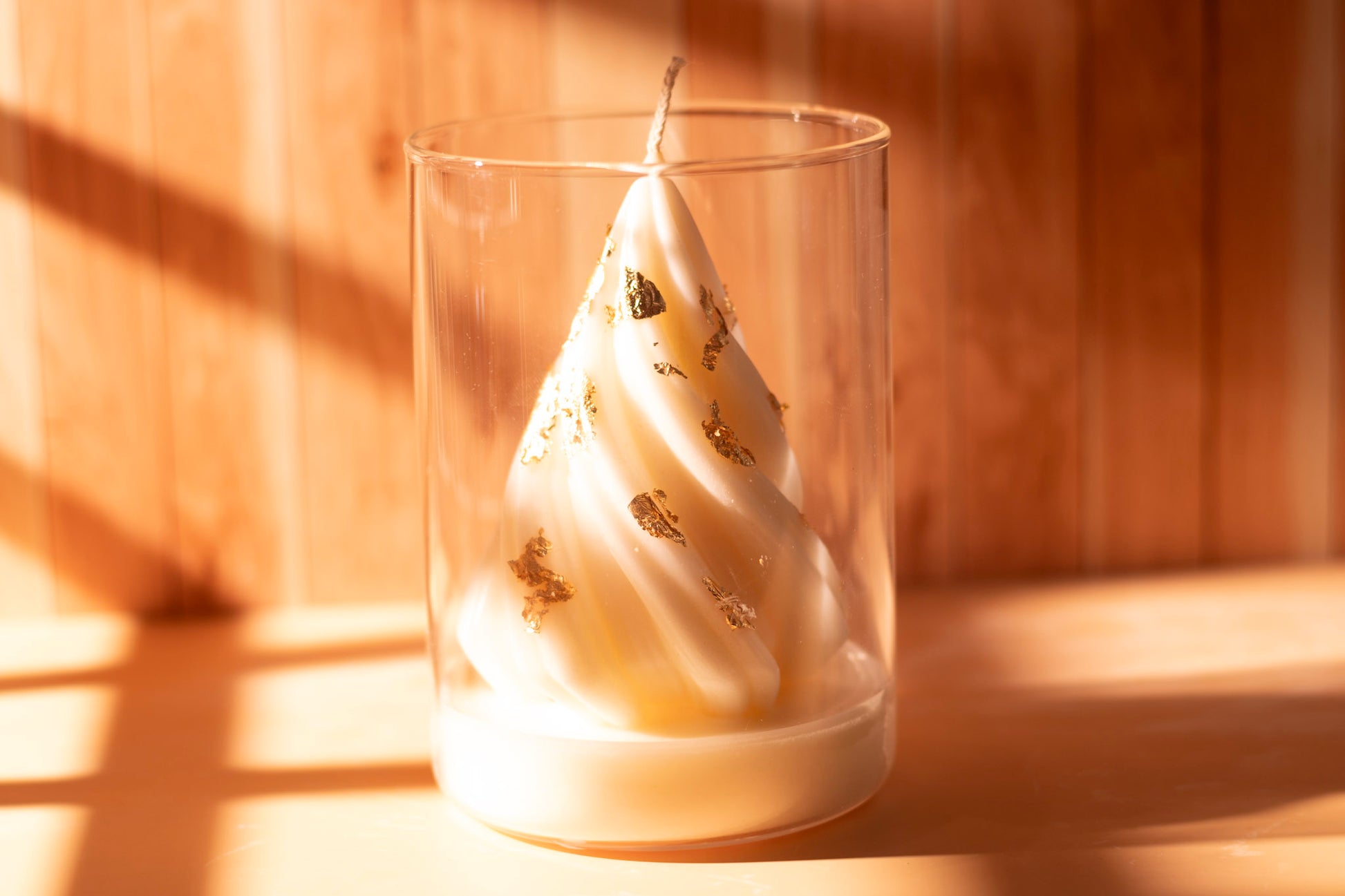 White sculpted Christmas tree candle with gold leaf accents in a clear glass jar, photographed in warm light on a wooden background