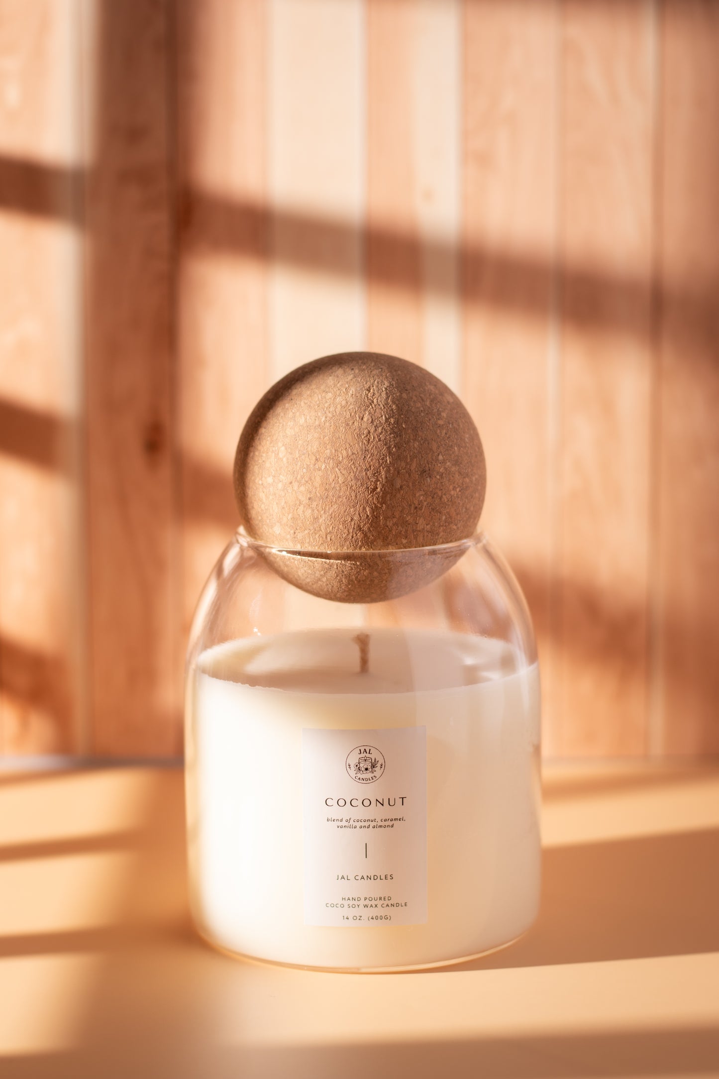 Hand-poured coconut soy candle with wooden lid by JAL Candles, photographed in warm sunlight on a wooden surface, made in Cyprus.