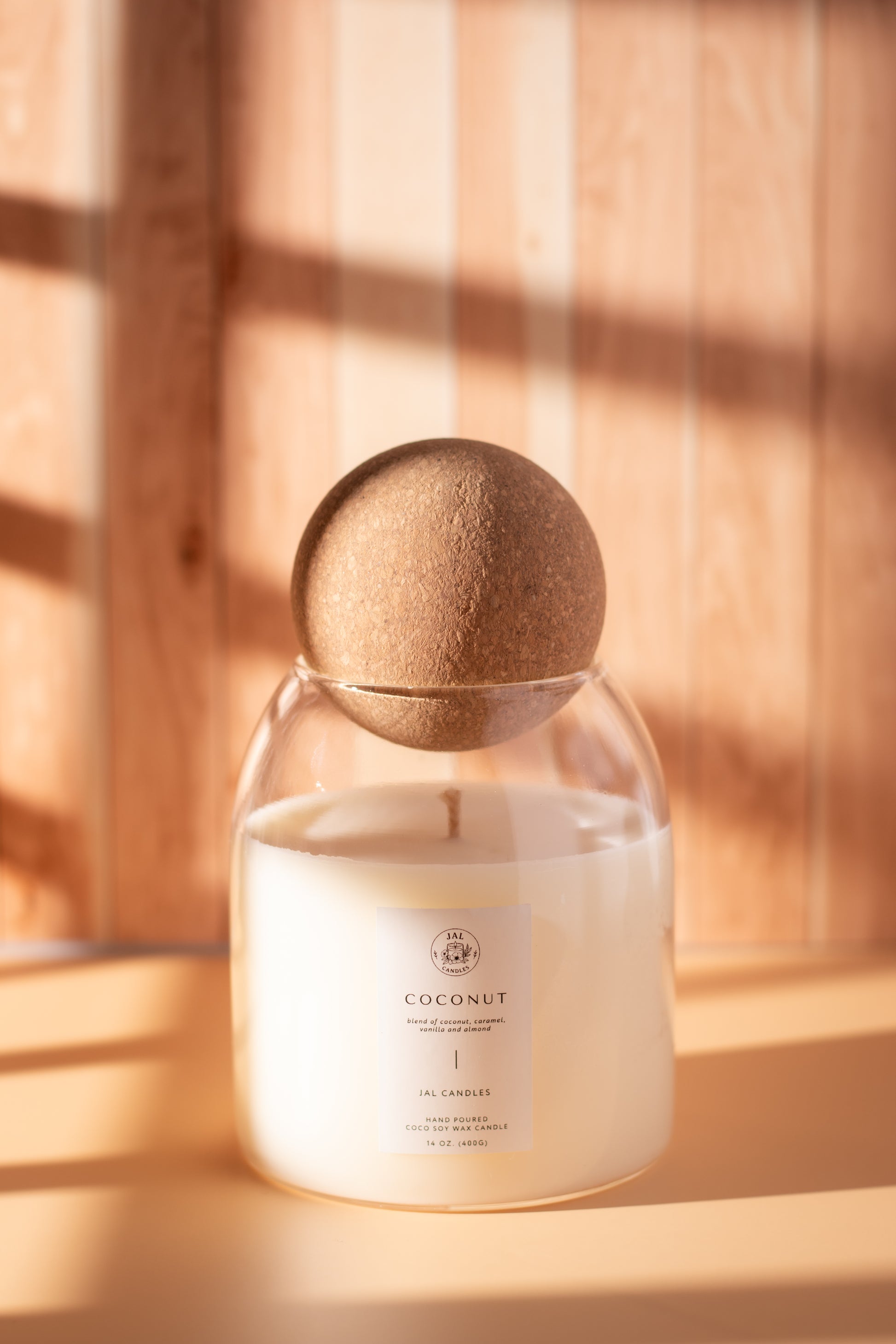 Hand-poured coconut soy candle with wooden lid by JAL Candles, photographed in warm sunlight on a wooden surface, made in Cyprus.