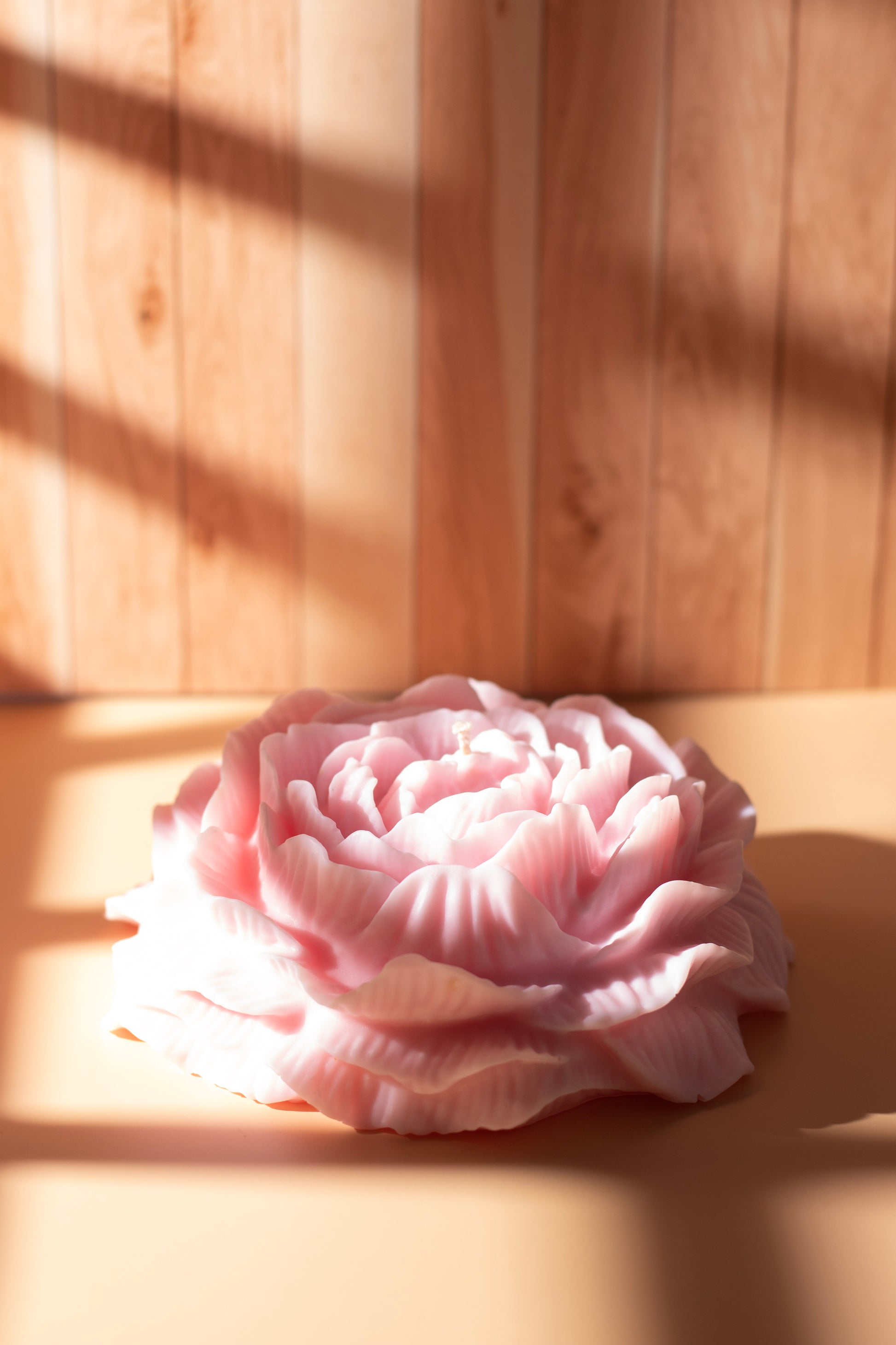 Hand-poured pink peony flower candle by JAL Candles, sculpted from soy wax and displayed in soft sunlight on a wooden background, made in Cyprus.