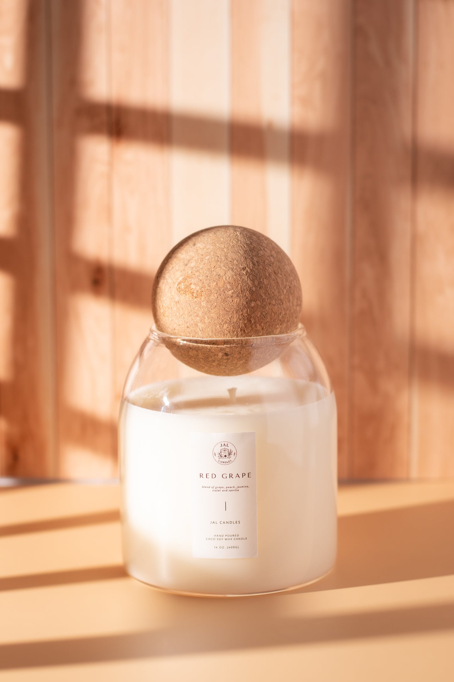 Hand-poured red grape candle with wooden lid by JAL Candles, photographed in warm sunlight on a wooden surface, crafted in Cyprus.