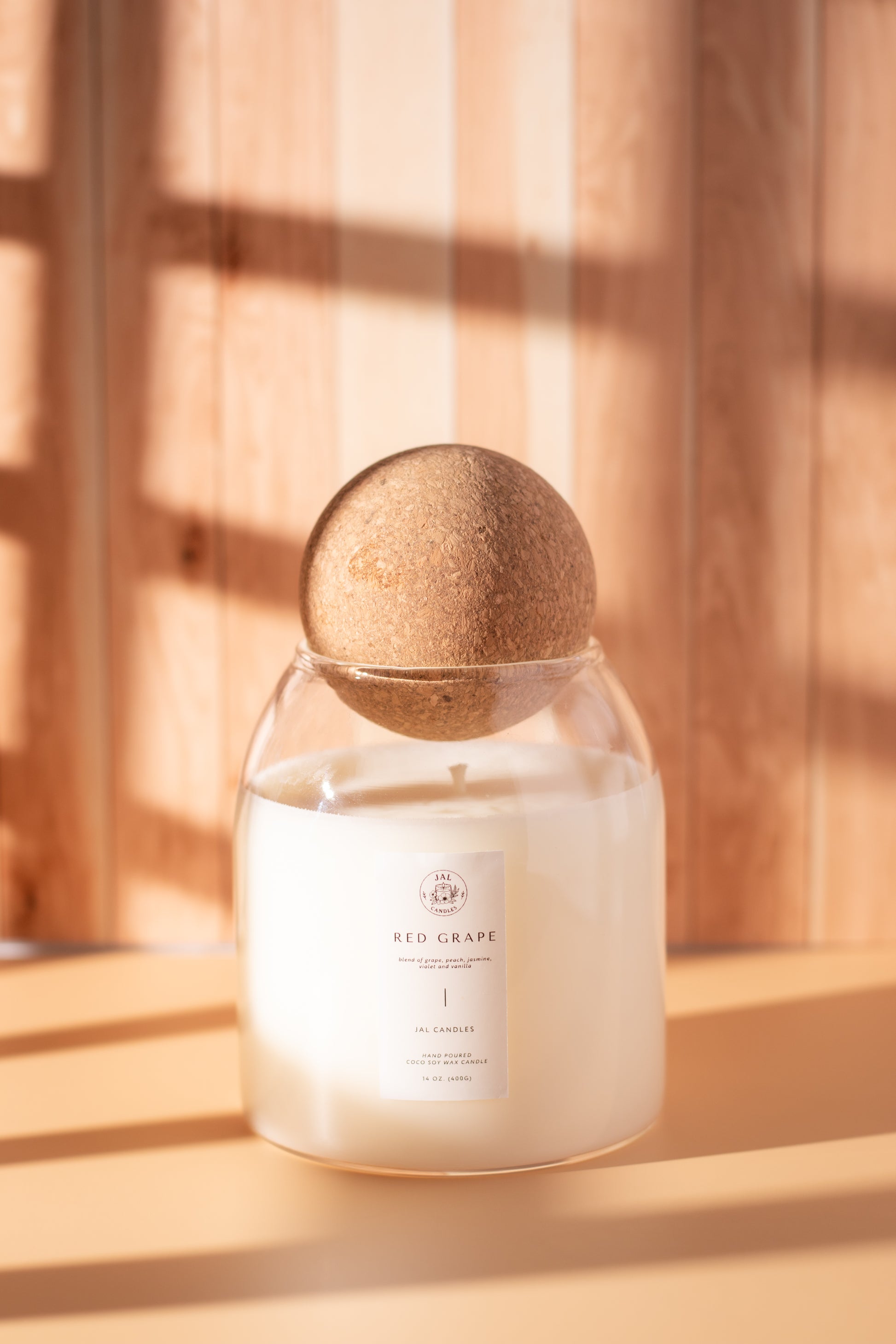 Hand-poured red grape candle with wooden lid by JAL Candles, photographed in warm sunlight on a wooden surface, crafted in Cyprus.