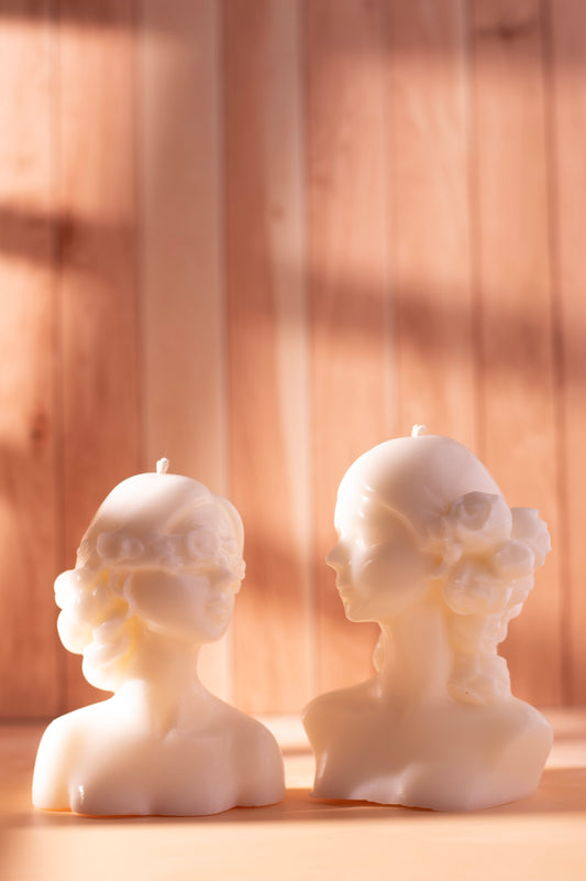 Two ivory female bust candles — one flower-blindfolded, one with roses in hair