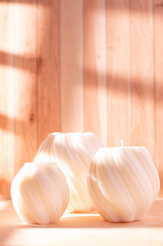 Three cream spiral-swirl sculpted candles in mixed sizes on wood surface
