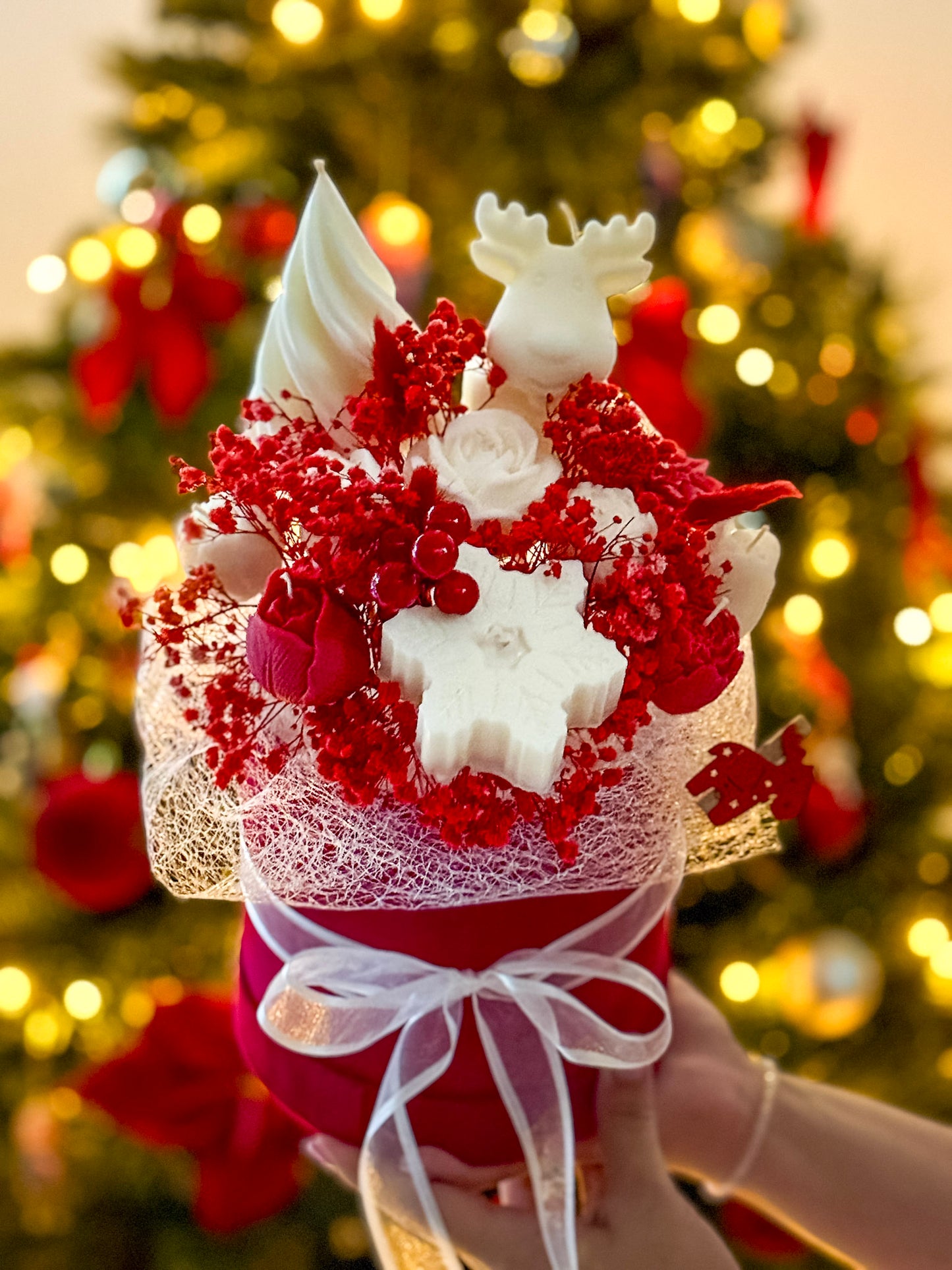 Handheld Reindeer's Wonderland handmade Christmas candle bouquet with red wax candles, white snowflake and reindeer decorations, golden bokeh lights background